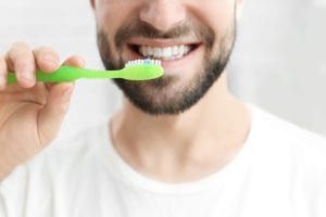 Close up of a man brushing his teeth with a green toothbrush